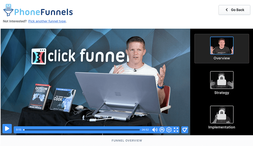 Russell Brunson sits at a desk with books and a laptop, giving a presentation about ClickFunnels application funnel overview. On the right, a menu shows Overview selected, with Strategy and Implementation locked.